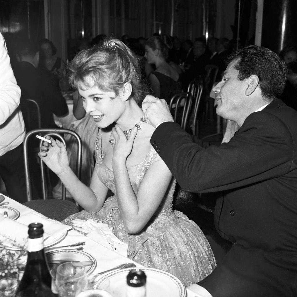 Gabriele Ferzetti buckling a necklace around Brigitte Bardot's neck, Italy, 1956 (b/w photo)